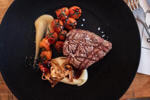 Beef tenderloin with rustic mashed potatoes, roasted cherrys and confit garlic sauce on dark plate photo