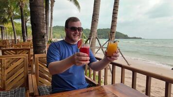 alegre hombre disfrutando tropical bebidas a un junto a la playa bar con palma arboles y Oceano en el fondo, encarnando vacaciones ocio y verano vibraciones video