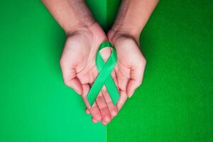 Jade tape in support of patients with hepatitis B and hepatocellular carcinoma. Green ribbon on female hands on grass background photo