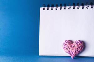Simple blue background with a small purple red heart yn notebook. Place for text photo