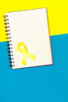 Golden ribbon for children as a symbol of childhood cancer awareness on a white notepad. World Cancer Day. photo