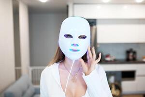 Portrait of a beautiful woman performing a light therapy facial mask procedure at home. photo
