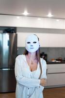 Portrait of a beautiful woman performing a light therapy facial mask procedure at home. photo