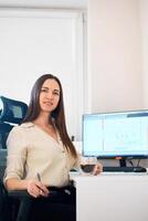 Portrait of a remote worker. A beautiful woman sits at a table in front of a computer and designs a building. Confident young lady freelancer working from home. photo