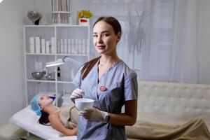 Happy female cosmetologist prepares the drug. Portrait pretty woman wearing white gloves and uniform. Beauty, cosmetology concept. photo