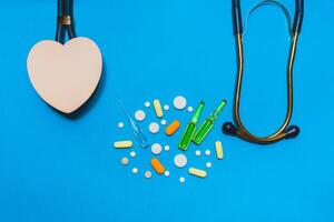 Medicine pills and other equipment of a doctor stethoscope as well as a red heart on a blue background. photo