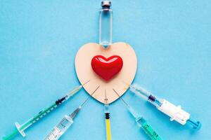 Volumetric heart shape with a set of different syringes on a blue background. The concept of supporting patients with acquired heart defects photo
