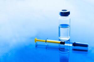 Vials of medication and syringe on a blue glass table with window background photo