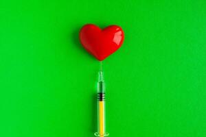 Volumetric heart shape with a syringe on a green background. Congenital heart defect photo