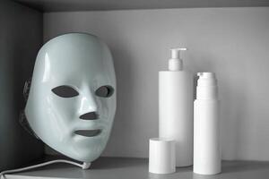 Light therapy LED mask on a shelf next to facial skin care products. photo