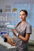 Happy female cosmetologist holding box with hands. Portrait pretty woman wearing white gloves and uniform, showing small box. Beauty, cosmetology concept. photo