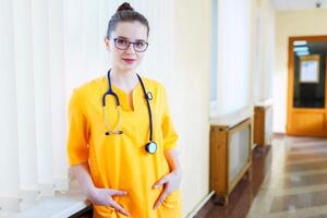 Doctor beautiful girl smiling. portrait in yellow uniform with a stethoscope to the corridor of the hospital. Health care. background photo