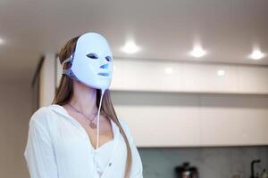 Beautiful woman getting a led light therapy mask treatment for her face at home. photo