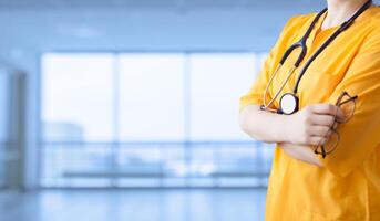 medicine advertisement. Young beautiful girl in yellow coat with stethoscope and with arms crossed hospital. An impersonal wide background. photo