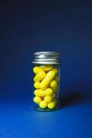 Bottle of clear glass with yellow pills on a blue background close-up vertical photo