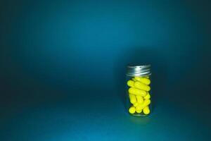 hospital drug concept. Yellow capsules in a transparent glass bottle of medium size, isolated on a dark background. Natural supplements for health. Studio lighting photo