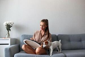 A creative female artist with a dog is sitting and working on a painting. A happy young lady is painting on canvas in her apartment. The concept of a young mother's leisure photo