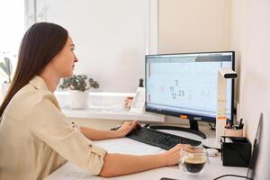 Portrait of a happy female designer estimator sitting at the table with a notebook and calculator, counting the balance and typing on a laptop, finishing her work with a cup of coffee. photo