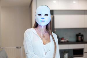 retrato de un hermosa mujer ejecutando un ligero terapia facial máscara procedimiento a hogar. foto