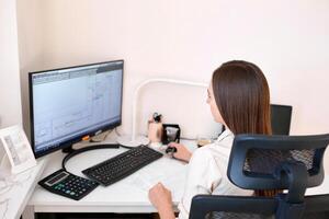 Portrait of a remote worker. A beautiful woman sits at a table in front of a computer and designs a building. Confident young lady freelancer working from home. photo