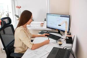 Portrait of a remote worker. An adult woman sits at a table in front of a computer and draws up a costly estimate. Confident young lady freelancer working from home. photo