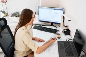 Portrait of a remote worker. An adult woman sits at a table in front of a computer and draws up a costly estimate. Confident young lady freelancer working from home. photo