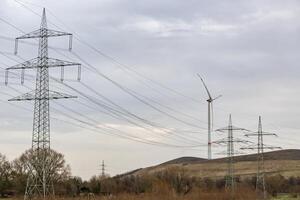 Alto voltaje pilones con viento turbina en alemán industrial paisaje foto