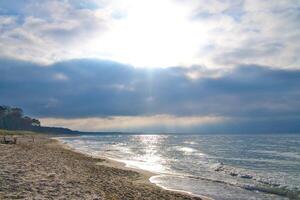 Sunset on the west beach on the Baltic Sea. Waves, beach, cloudy sky and sunshine photo