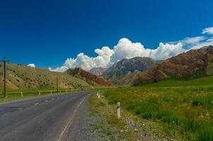 un sereno paisaje, con verde campos debajo un azul cielo, flanqueado por majestuoso montañas y un serpenteante la carretera. foto