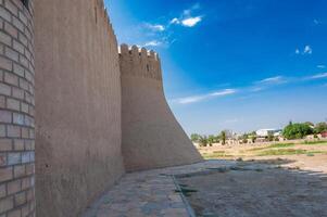 Imposing ancient fortress walls and a corner tower, featuring traditional crenellations, stretch towards the sky, juxtaposed with contemporary structures in the surrounding urban landscape. photo