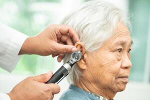 Audiologist or ENT doctor use otoscope checking ear of asian senior woman patient treating hearing loss problem. photo