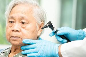 Audiologist or ENT doctor use otoscope checking ear of asian senior woman patient treating hearing loss problem. photo