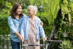 Doctor caregiver help and care Asian senior woman patient walk with walker in park at hospital. photo