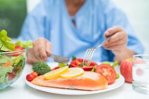 Asian elderly woman patient eating salmon steak breakfast with vegetable healthy food in hospital. photo