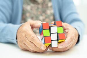 Bangkok, Thailand August 14, 2023 Alzheimer disease AD, Asian elderly woman patient playing Rubik cube game to practice brain training for dementia prevention. photo