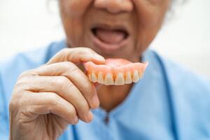 paciente anciana asiática sosteniendo para usar dentadura postiza, concepto médico fuerte y saludable. foto