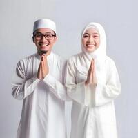 AI generated Heartwarming portrayal of a young Asian Muslim couple in traditional attire, including hijab, exchanging joyful Eid Mubarak gestures in a studio setting with a neutral color palette photo