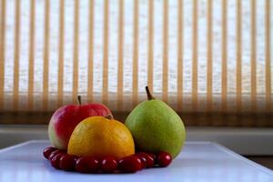 Ripe pear, orange and apple with laid out berries around on rattan curtains background photo