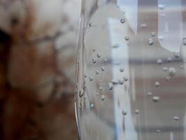 Side of a glass with lightly carbonated mineral water and a few bubbles on blurred backdrop photo