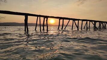 Old wooden pier silhouette against a tranquil ocean at sunset, evoking a serene, peaceful summer evening video