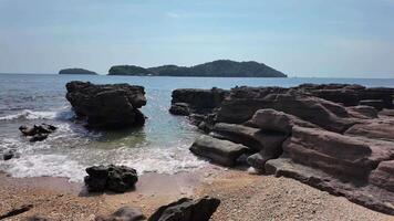 escabroso costero paisaje con olas suavemente estrellarse en contra rocoso costa, con vista a sereno islas en un soleado día, Perfecto para viaje y naturaleza temática contenido video