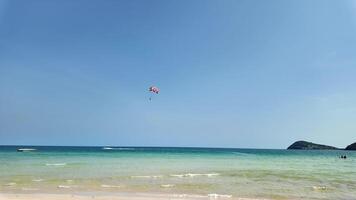 panoramico tropicale spiaggia con chiaro blu cieli, un' paracadute ascensionale nel il distanza, e motoscafi vicino il costa, Perfetto per viaggio e estate vacanza temi video