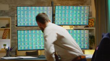 Bearded broker in his home office wearing a suits checking the stock market on four displays video