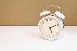 White alarm clock on a white table and brown background. photo