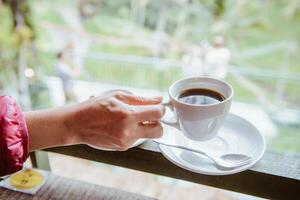 Woman hand holding a cup of hot Luwak coffee, one of the most expensive coffee in the world in the coffee shop in Bali, Indonesia. photo