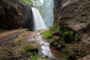 Scenery view of Blawan waterfall located in Kalianyar village, Sempol district of East Java, Indonesia. Blawan waterfall is surrounded by sharp cliffs and there is also stalagmite cave. photo