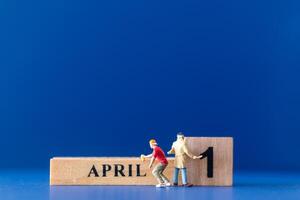 Miniature people painting a wooden block on April 1st photo