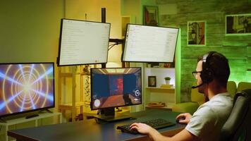 Young man enertaning himself playing shooter game on computer with multiple monitors. video