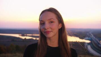 retrato do uma sorridente jovem menina contra uma pôr do sol fundo. video