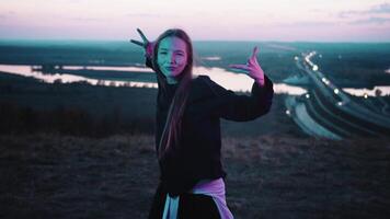 jovem menina é dançando às crepúsculo, contra a fundo do uma ponte sobre uma rio. video
